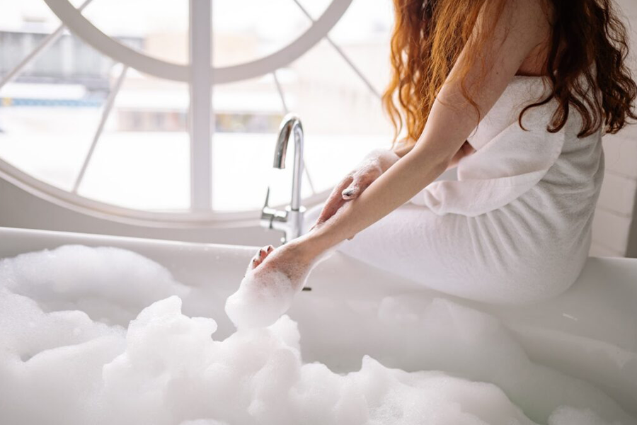 Person in white bath towel sitting on white bathtub