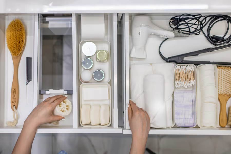 Woman organizing bathroom amenities and toiletries in drawer in bathroom