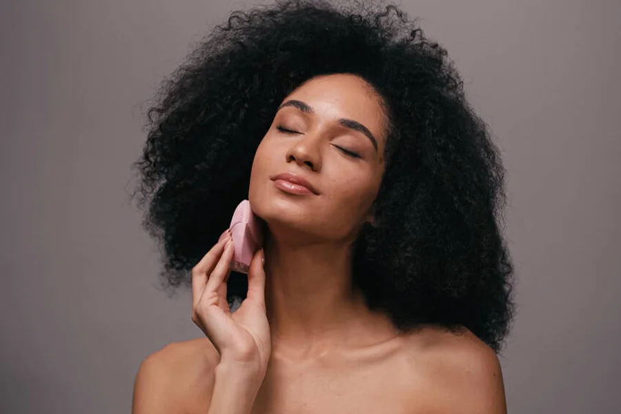 Woman using a pink facial cleansing brush around the jawline