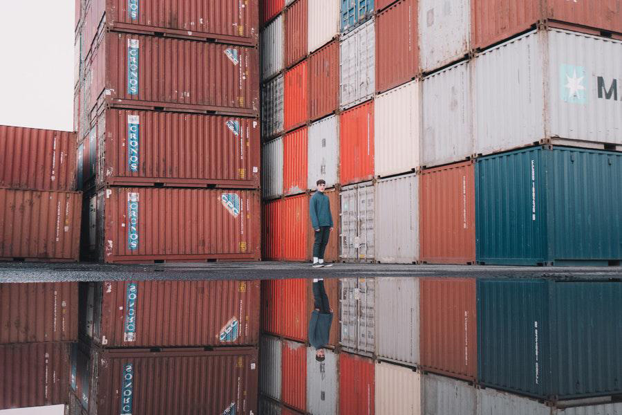 Man in green top and pants standing beside shipping containers