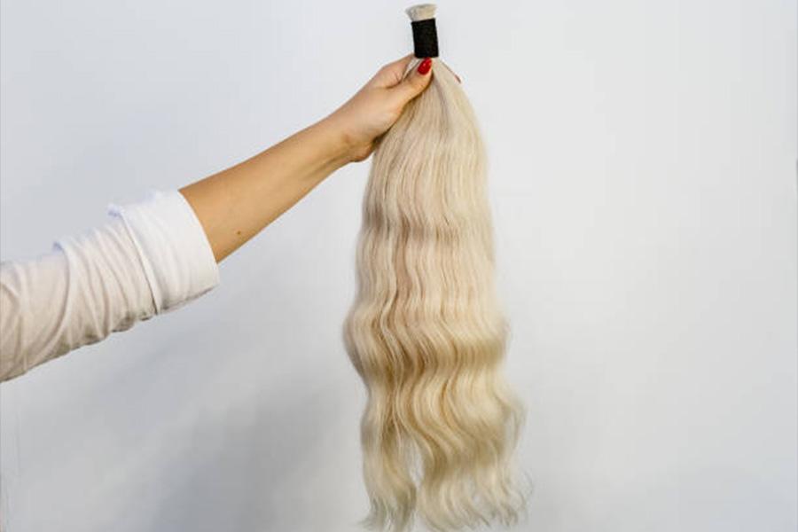 Mujer sosteniendo una extensión de cabello rubio contra la pared blanca