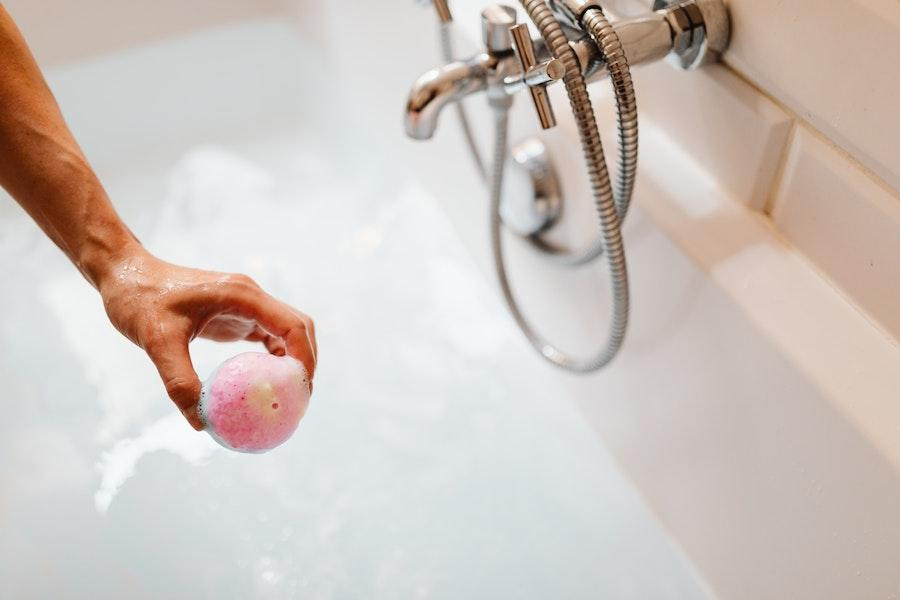 Hand holding bath bomb over tub