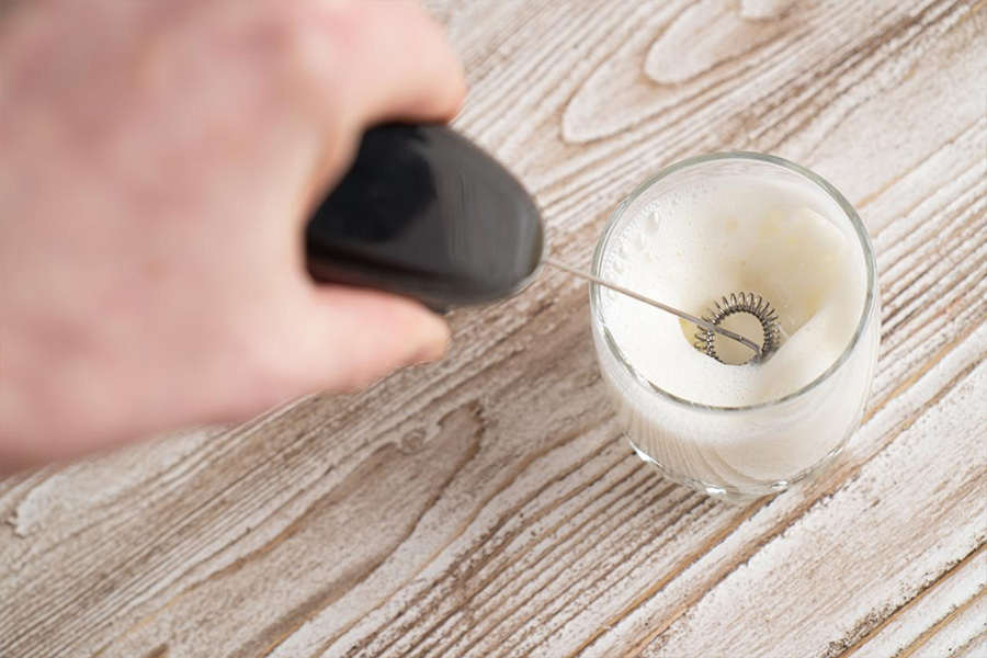 person using milk frother to create coffee drink at home