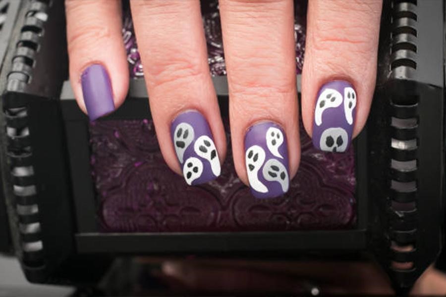 Uñas de mujer pintadas de morado con fantasmas blancos encima