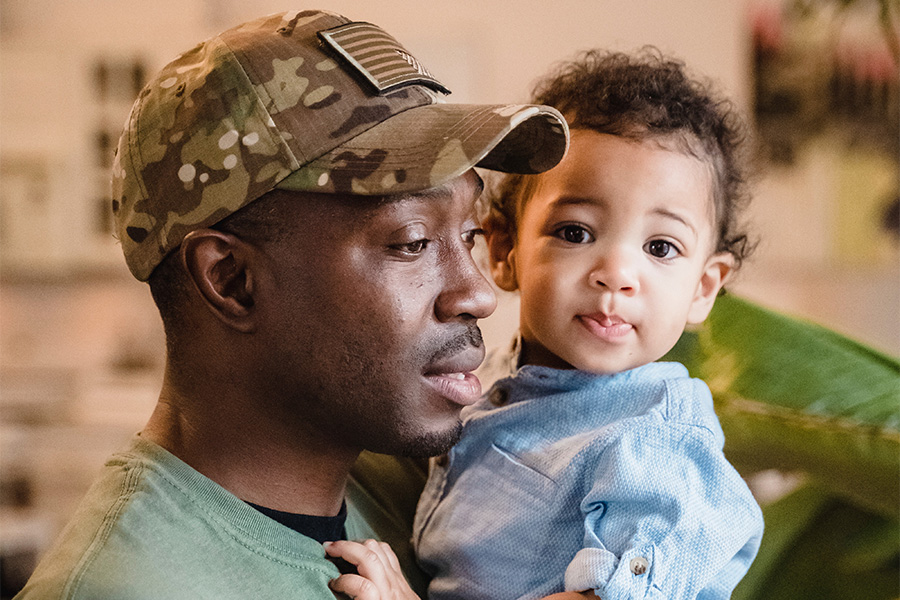 man carrying a child while wearing a camo trucker hat