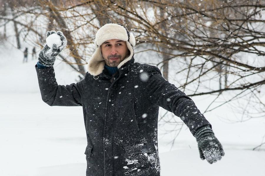 Homme tenant une boule de neige tout en secouant un chapeau de trappeur