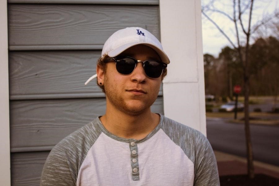 Man posing with shades and a white baseball cap