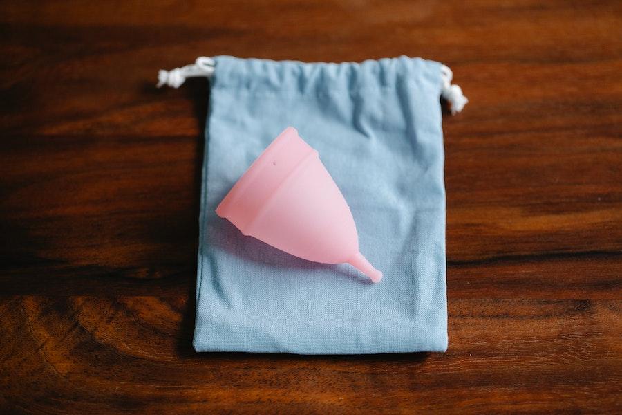 Copo de menstruação reutilizável rosa em um saco azul