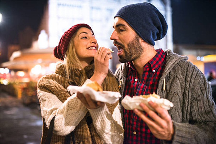 Woman feeding man both wearing beanies