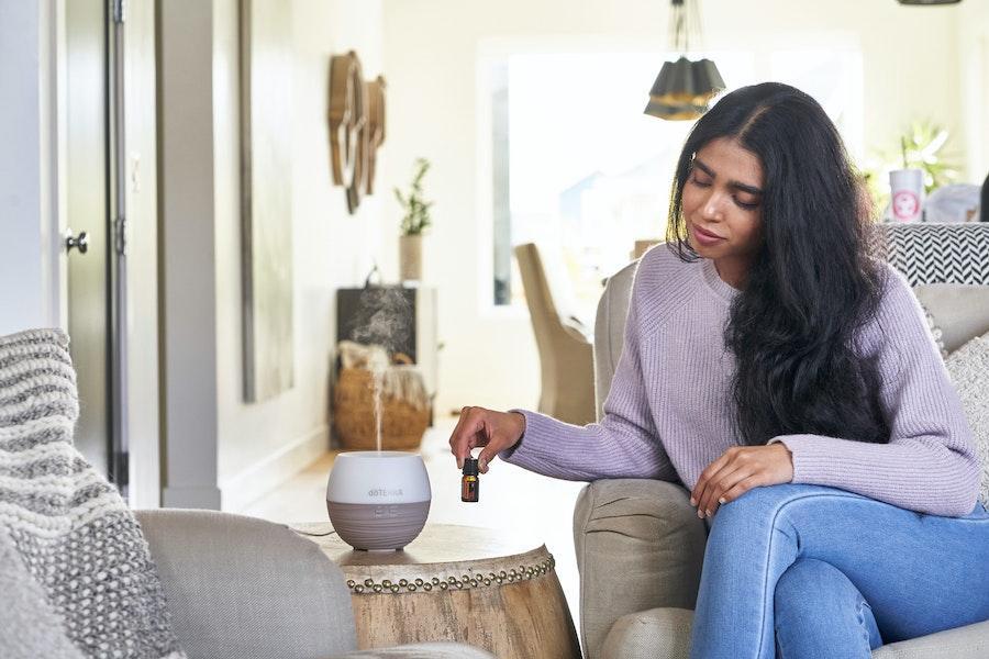 Woman placing fragrance oil near an aroma diffuser