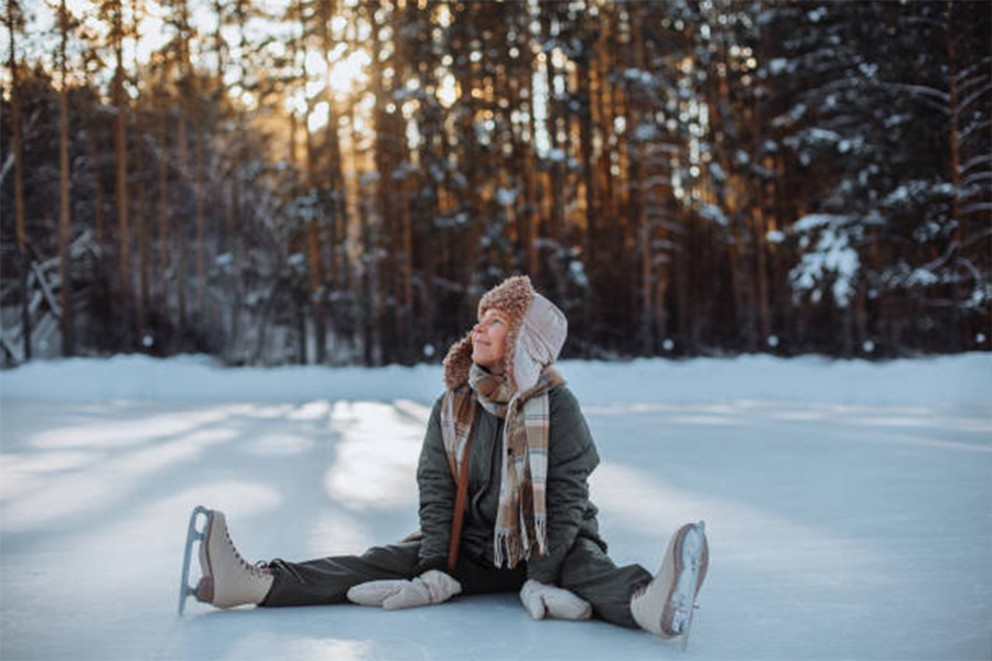 Woman sitting on the ice in skates with trapper hat