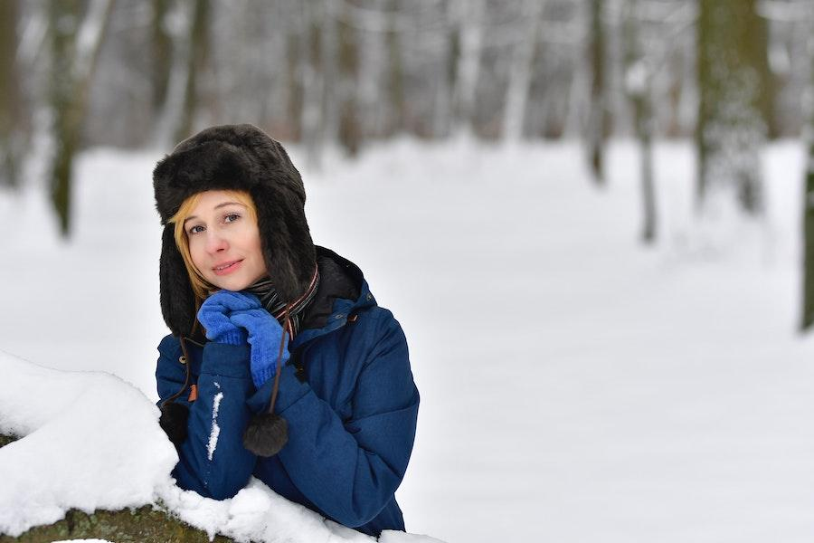 黒い罠猟帽をかぶって雪の上に座る女性