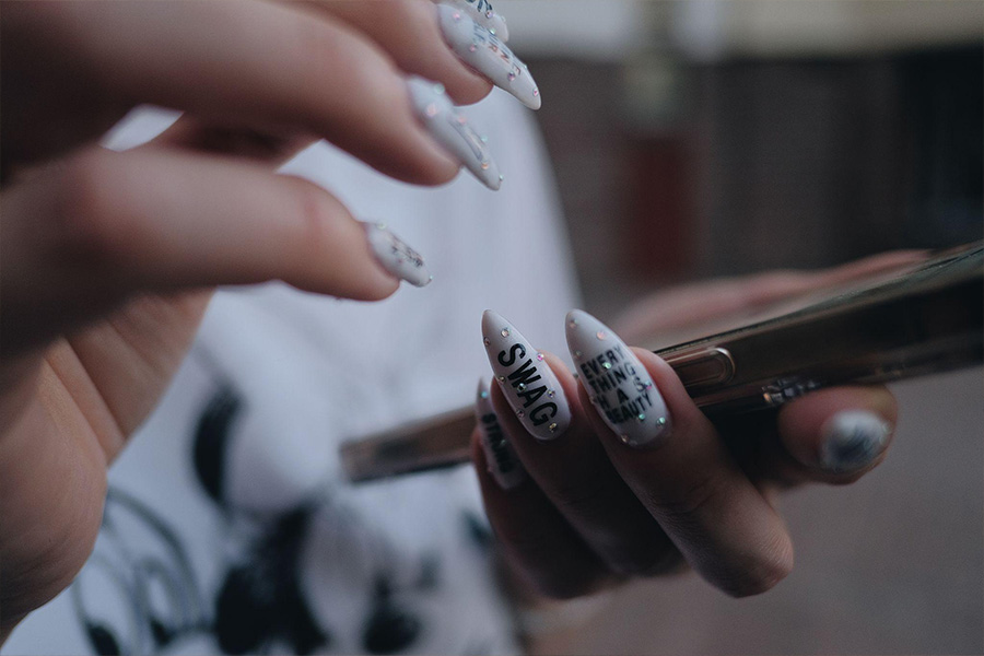 Woman's acrylic nails with rhinestones and text.