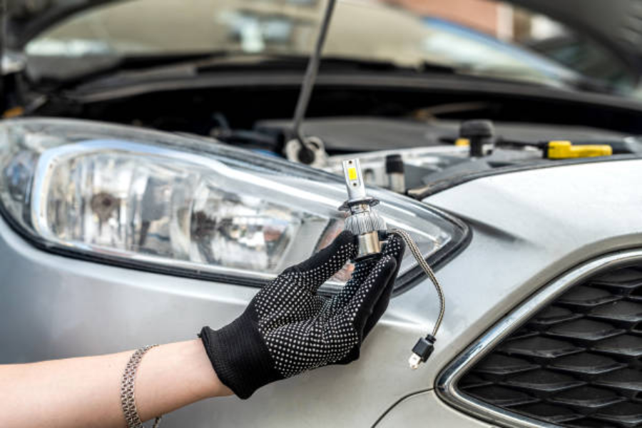 Una mano che tiene una moderna lampadina a LED vicino al faro di un'auto