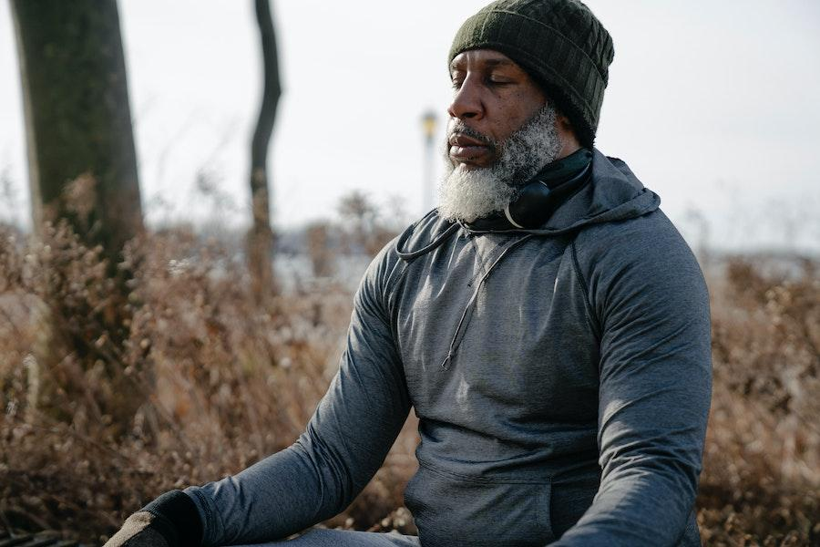 Hombre meditando con una sudadera con capucha gris y un gorro