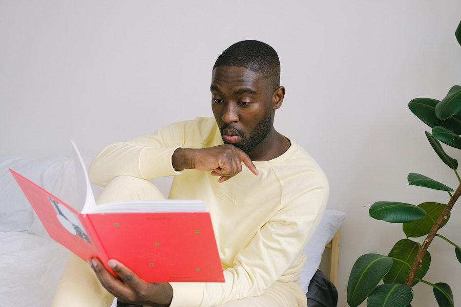 Hombre leyendo un libro rojo mientras usa pijama amarillo