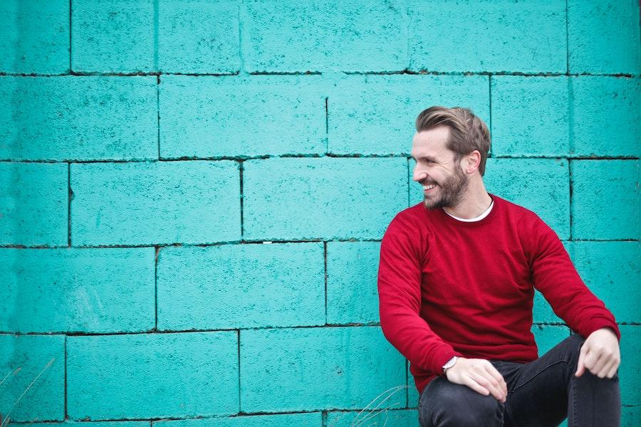 Hombre sonriendo de lado con una sudadera roja y un traje de jeans