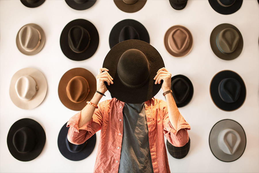 Un hombre parado en una habitación llena de sombreros fedora.