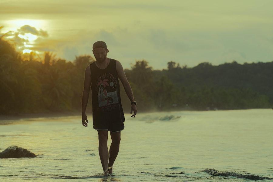 Hombre caminando en una playa mientras usa una camiseta sin mangas gráfica