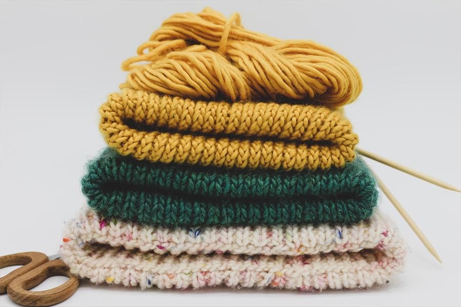 Pile de chapeaux tricotés avec du fil, des aiguilles et des ciseaux