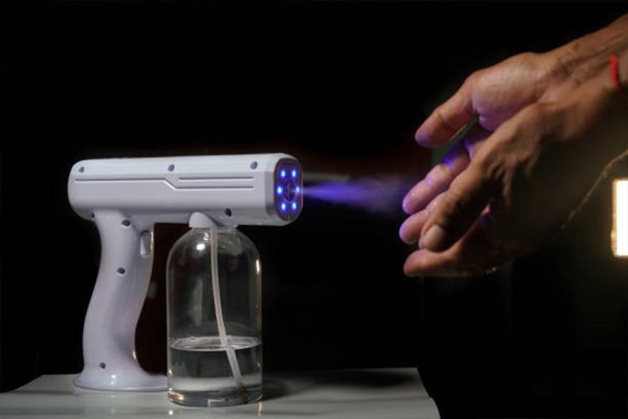 White hand sanitizer gun spraying mist onto hands