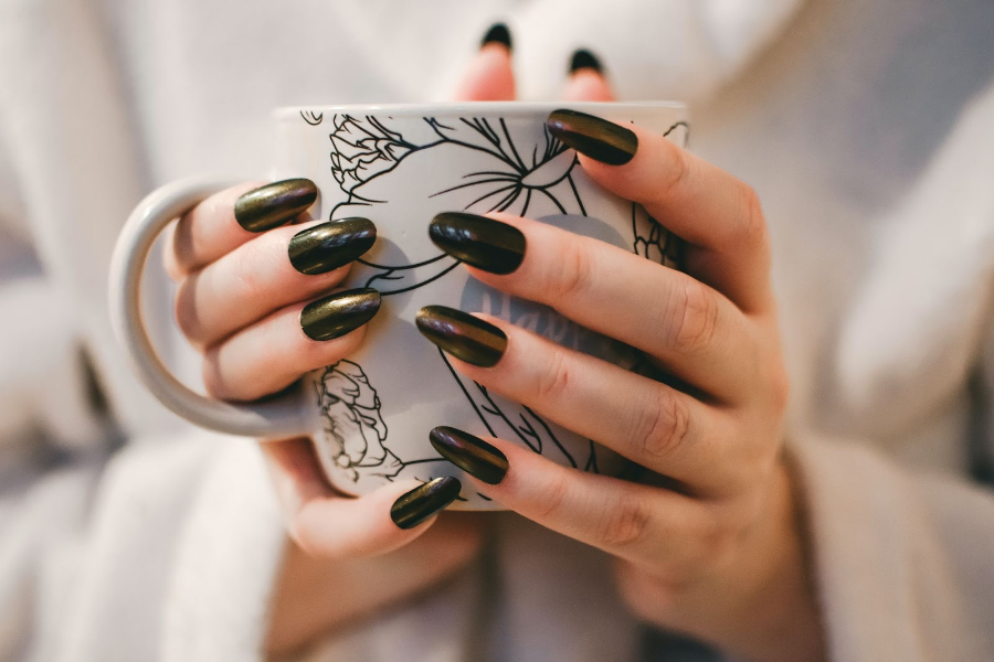 Woman holding cup and showing dark nails