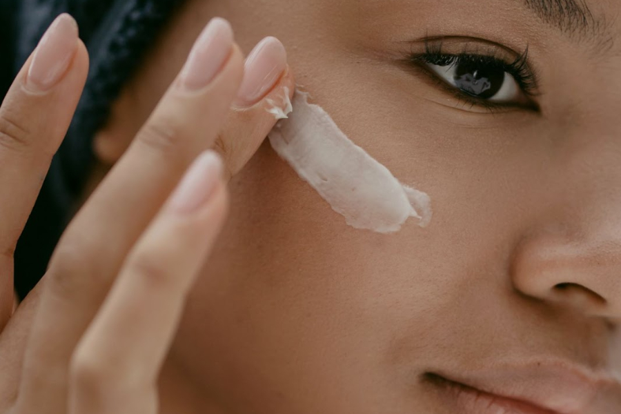 Mulher com unhas vermelhas aplicando produtos para a pele